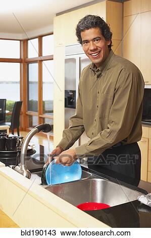 Stock Image - Man washing dishes in kitchen. Fotosearch
