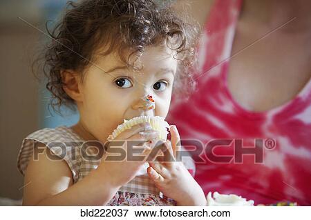 Stock Photo - Messy baby girl eating cupcake. Fotosearch