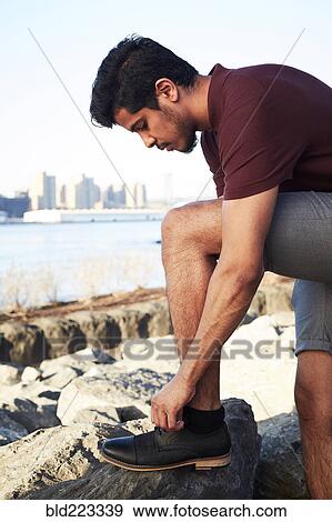Stock Photo - Middle Eastern man tying shoelace at waterfront. Fotosearch