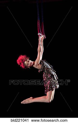 Stock Image - Mixed race acrobat hanging from trapeze. Fotosearch