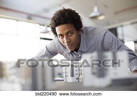 Stock Image - Mixed race architect examining architectural model in office. Fotosearch