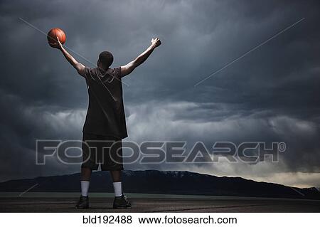 Stock Photo - Mixed race basketball player standing with storm clouds in distance. Fotosearch