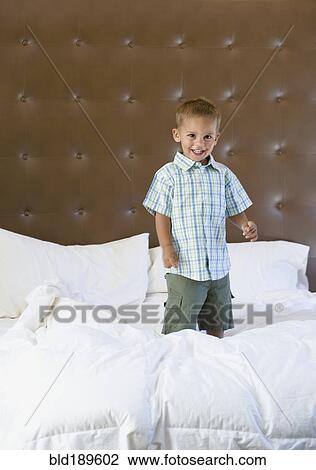 Stock Image - Mixed race boy jumping on bed. Fotosearch