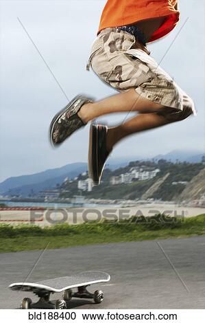 Stock Image - Mixed Race boy jumping over skateboard. Fotosearch