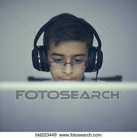Stock Photo - Mixed Race boy listening to laptop with headphones. Fotosearch