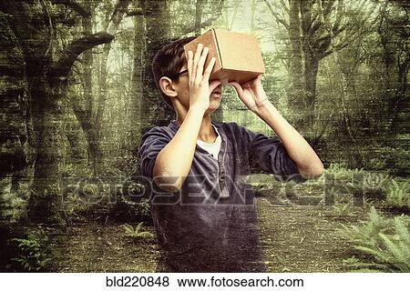 Stock Photo - Mixed race boy peering in box in forest. Fotosearch