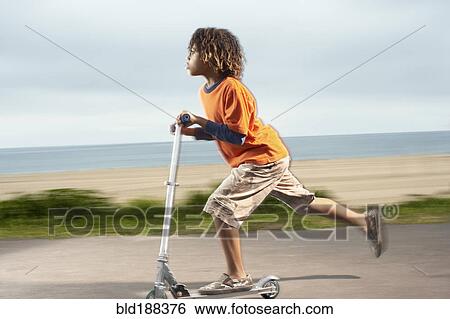 Stock Photograph - Mixed Race boy riding foot-powered scooter. Fotosearch