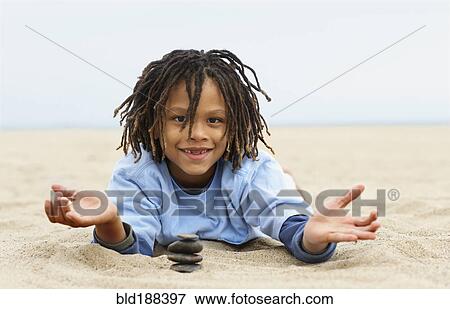 Stock Photo - Mixed Race boy stacking stones on sand. Fotosearch