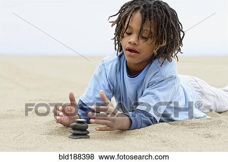 Stock Photo - Mixed Race boy stacking stones on sand. Fotosearch