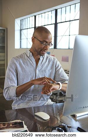 Mixed race businessman checking his watch in office View Large Photo Image Stock Photo - Mixed race businessman checking his watch in office. Fotosearch