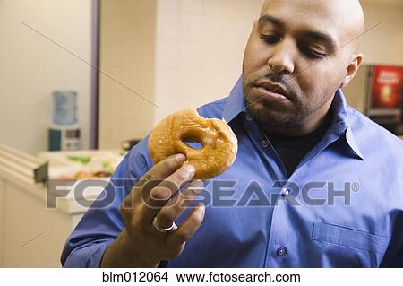Picture - Mixed race businessman eating donut in office. Fotosearch
