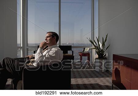 Stock Image - Mixed race businessman sitting in armchair and looking pensive. Fotosearch
