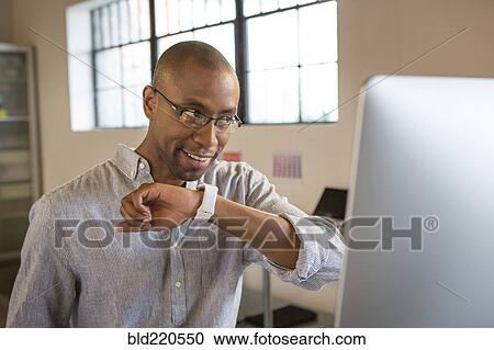 Stock Image - Mixed race businessman talking into smart watch in office. Fotosearch