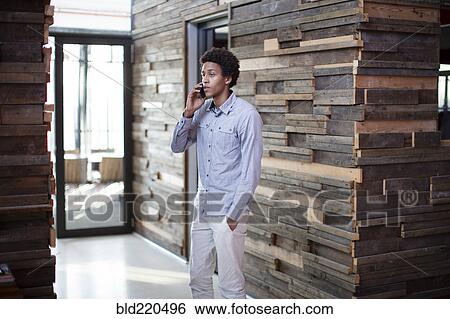 Stock Photograph - Mixed race businessman talking on cell phone in hallway. Fotosearch