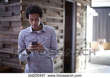Stock Photo - Mixed race businessman using cell phone in hallway. Fotosearch