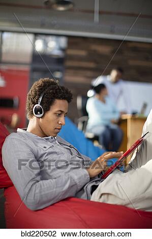 Stock Image - Mixed race businessman using digital tablet in office lounge. Fotosearch