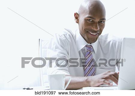 Stock Photo - Mixed race businessman using laptop at desk. Fotosearch