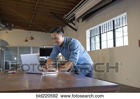 Stock Image - Mixed race businessman working on laptop in office. Fotosearch