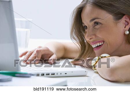 Stock Photo - Mixed race businesswoman laying on desk using laptop. Fotosearch
