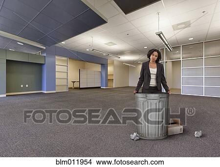 Picture - Mixed race businesswoman standing with garbage cans in empty office. Fotosearch