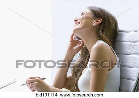 Picture - Mixed race businesswoman talking on cell phone at desk. Fotosearch