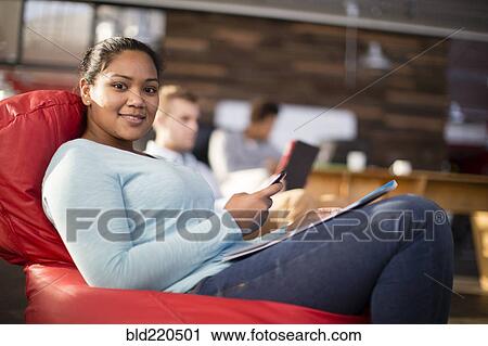 Stock Image - Mixed race businesswoman using cell phone in office lounge. Fotosearch