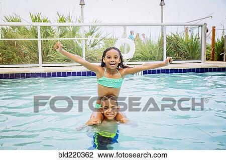 Stock Image - Mixed race children playing in swimming pool. Fotosearch