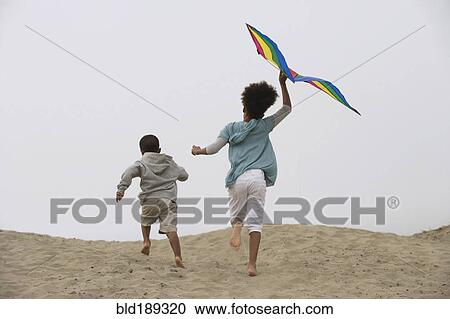 Stock Image - Mixed race children running on beach with kite. Fotosearch
