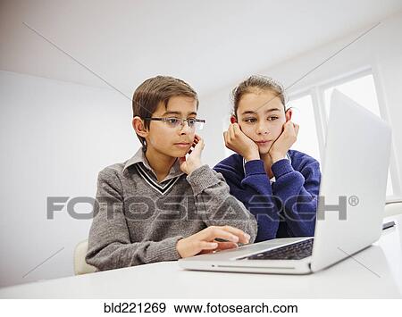 Stock Photo - Mixed race children using laptop at desk. Fotosearch