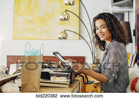 Stock Image - Mixed race clerk using register in shop. Fotosearch