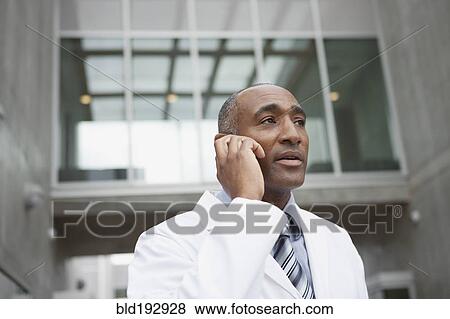 Stock Photo - Mixed race doctor talking on cell phone outdoors. Fotosearch