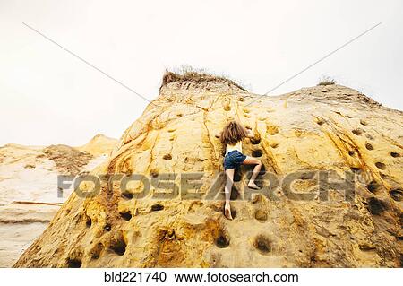 Stock Image - Mixed race girl climbing cliff rock. Fotosearch