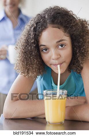 Picture - Mixed race girl drinking orange juice with straw. Fotosearch
