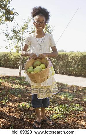 Stock Image - Mixed race girl holding basket of apples. Fotosearch