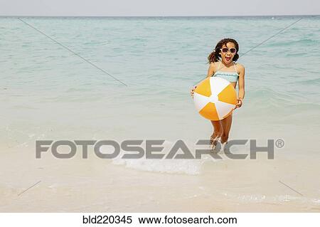 Stock Photography - Mixed race girl holding beach ball in ocean waves. Fotosearch