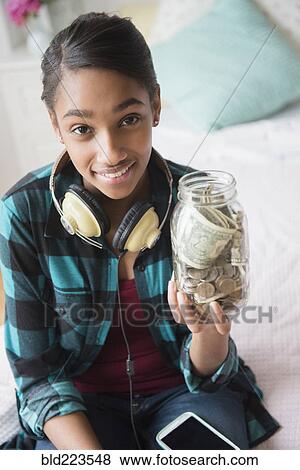 Stock Photo - Mixed Race girl holding jar containing cash and coins. Fotosearch