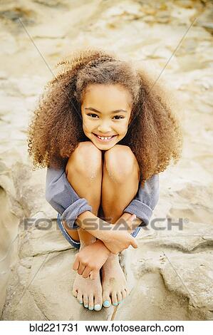 Stock Image - Mixed race girl hugging her knees. Fotosearch