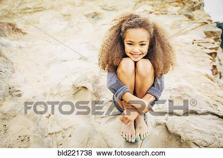 Stock Photo - Mixed race girl hugging knees on rock. Fotosearch