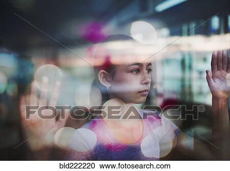 Stock Image - Mixed race girl looking out window. Fotosearch
