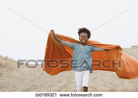 Stock Image - Mixed race girl playing with blanket at beach. Fotosearch