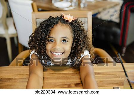 Picture - Mixed race girl sitting at restaurant table. Fotosearch