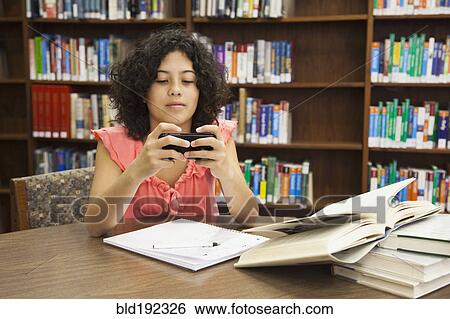 Stock Photograph - Mixed race girl text messaging on cell phone in library. Fotosearch