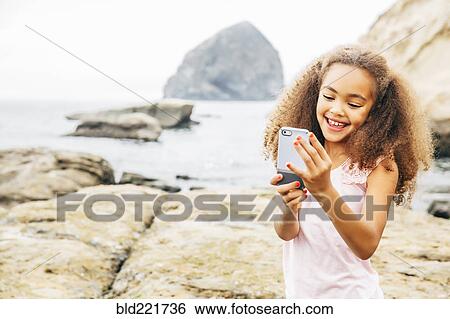 Stock Photograph - Mixed race girl using cell phone on beach. Fotosearch