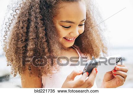Stock Photography - Mixed race girl using cell phone on beach. Fotosearch