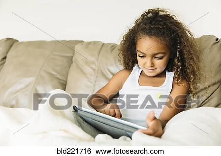 Mixed race girl using digital tablet on sofa View Large Photo Image Stock Photograph - Mixed race girl using digital tablet on sofa. Fotosearch