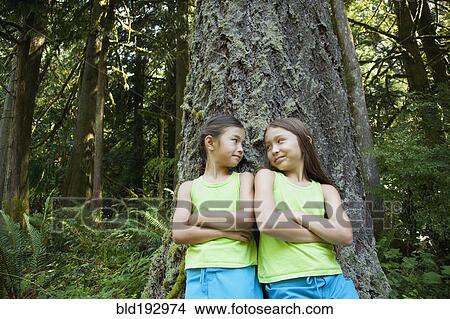 Picture - Mixed race girls leaning on tree. Fotosearch