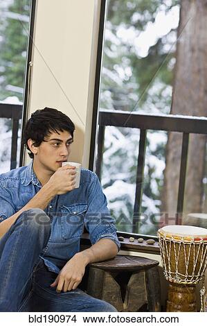 Mixed race man drinking coffee in living room View Large Photo Image Picture - Mixed race man drinking coffee in living room. Fotosearch
