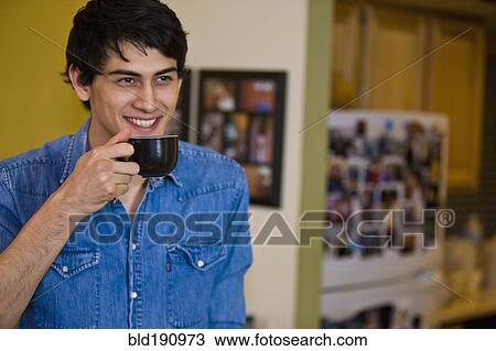 Stock Image - Mixed race man drinking coffee in kitchen. Fotosearch
