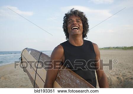 Mixed race man holding surfboard on beach View Large Photo Image Stock Image - Mixed race man holding surfboard on beach. Fotosearch