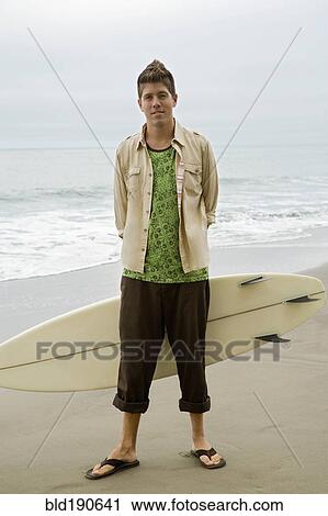 Stock Image - Mixed race man holding surfboard. Fotosearch